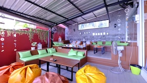 A cozy outdoor seating area with green cushioned benches and a wooden table, surrounded by potted plants and decorative items. - Chill Inn Beach Cafe & Hostel (Koh Samui)