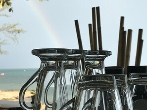 A row of clear glass pitchers with handles, placed outdoors with a beach and ocean view in the background. - Chill Inn Beach Cafe & Hostel (Koh Samui)