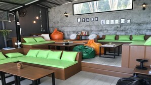 A lounge area with green cushioned seating, a coffee table, and a wall with framed pictures. - Chill Inn Beach Cafe & Hostel (Koh Samui)