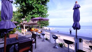 An outdoor seating area with a view of the sea, featuring wooden tables and chairs, a small bar area, and umbrellas. - Chill Inn Beach Cafe & Hostel (Koh Samui)