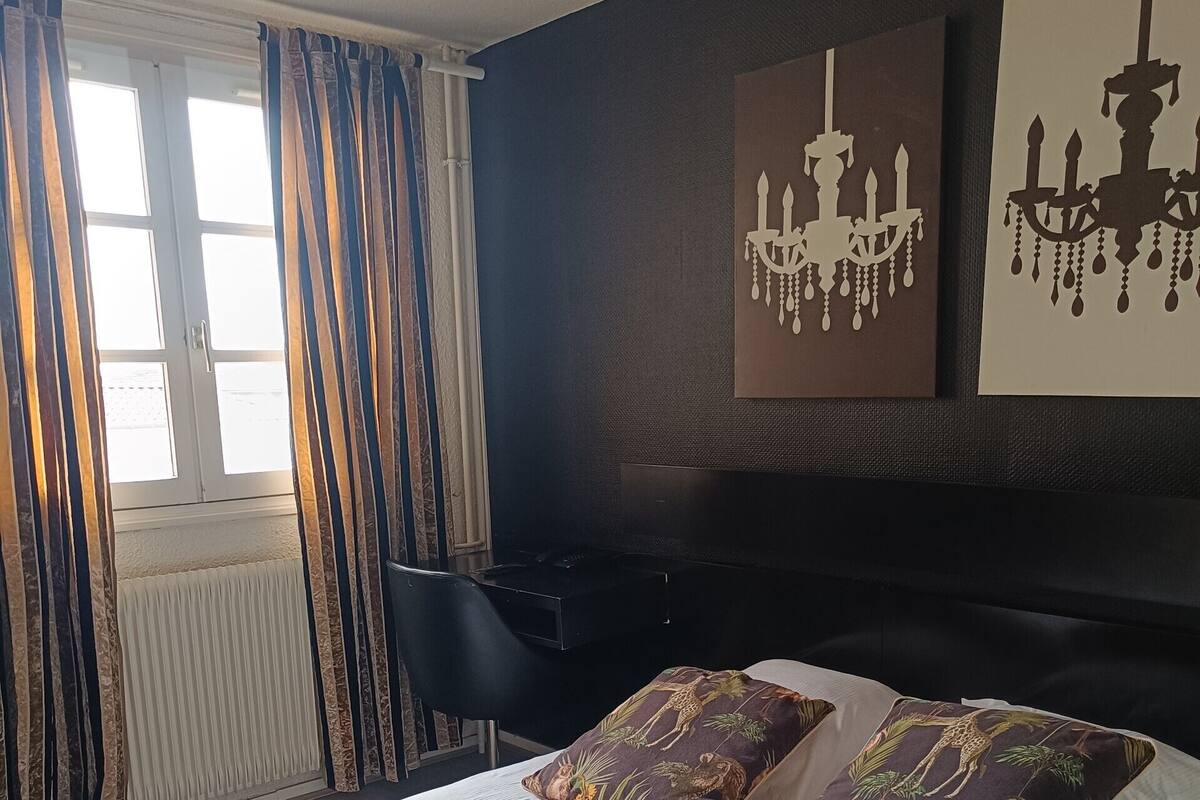 Ein Schlafzimmer mit einem großen Bett, zwei Zierkissen, einem schwarzen Kopfteil und einem Fenster mit Vorhängen.