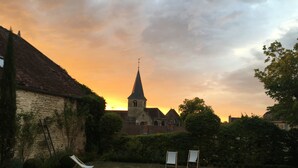 A courtyard with a church in the background, surrounded by greenery and two empty lounge chairs. - B&B Le Jardin de Carco (Chatillon-sur-Seine)