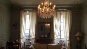 A room with a chandelier, a sofa, a table, and a mirror. - B&B Le Jardin de Carco (Chatillon-sur-Seine)