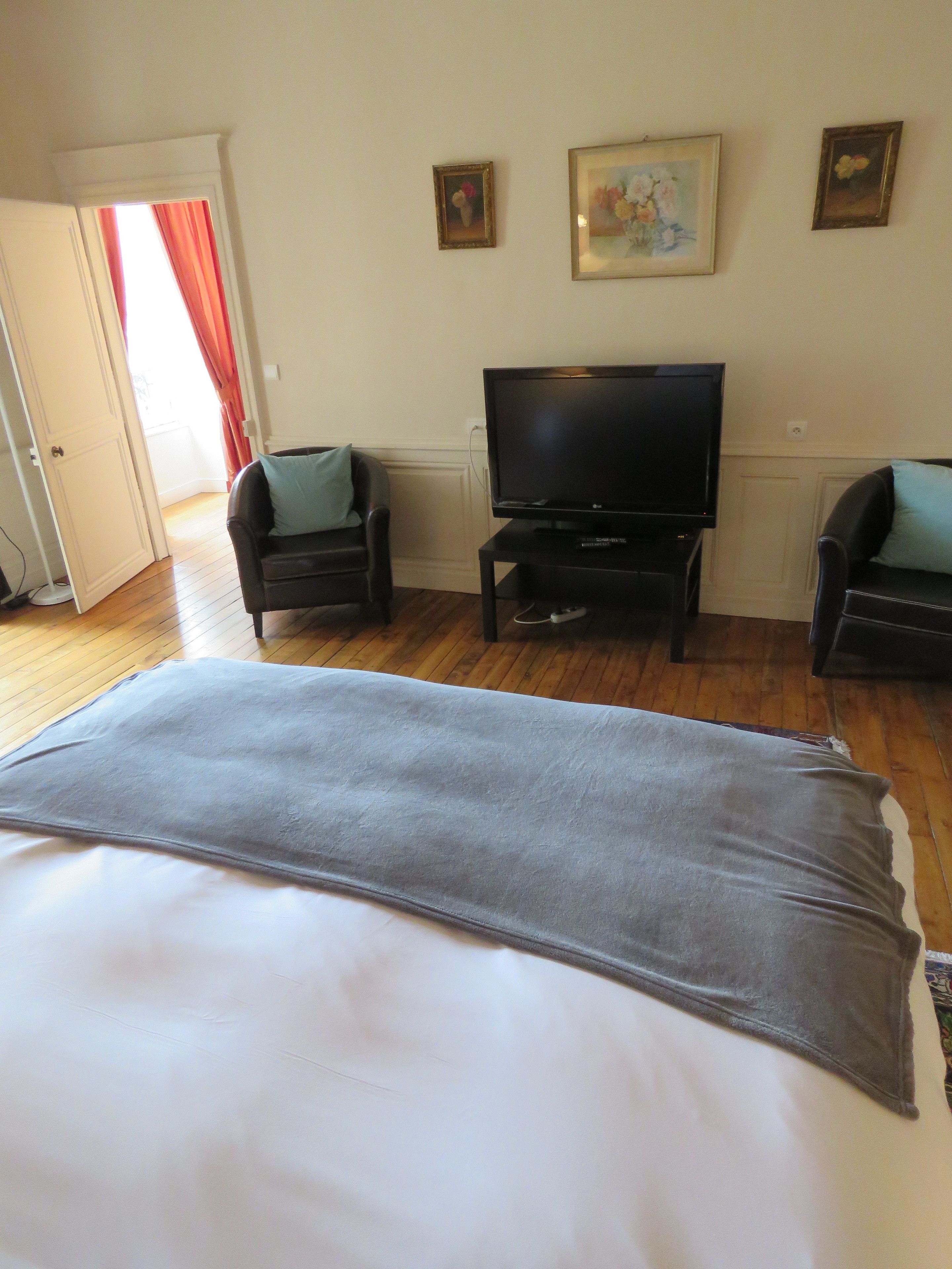 A bedroom with a bed, two chairs, a television, and three framed pictures on the wall.