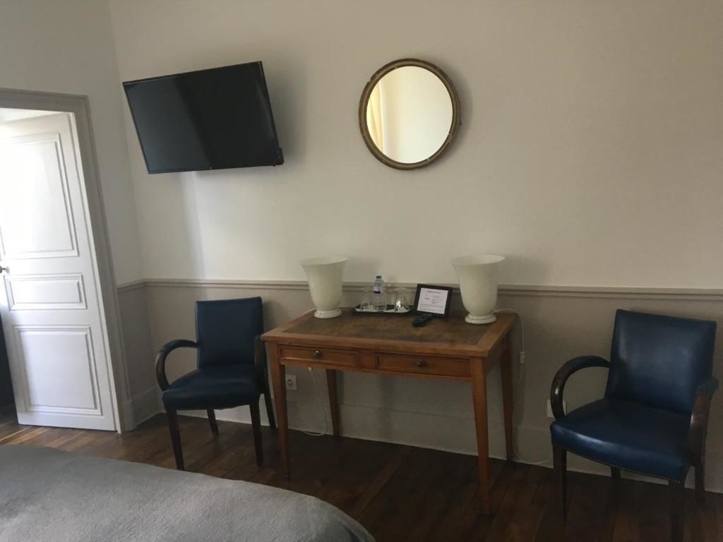 Een kamer met een bed, twee stoelen, een houten tafel met twee lampen, een flatscreen-tv en een ronde spiegel aan de muur.