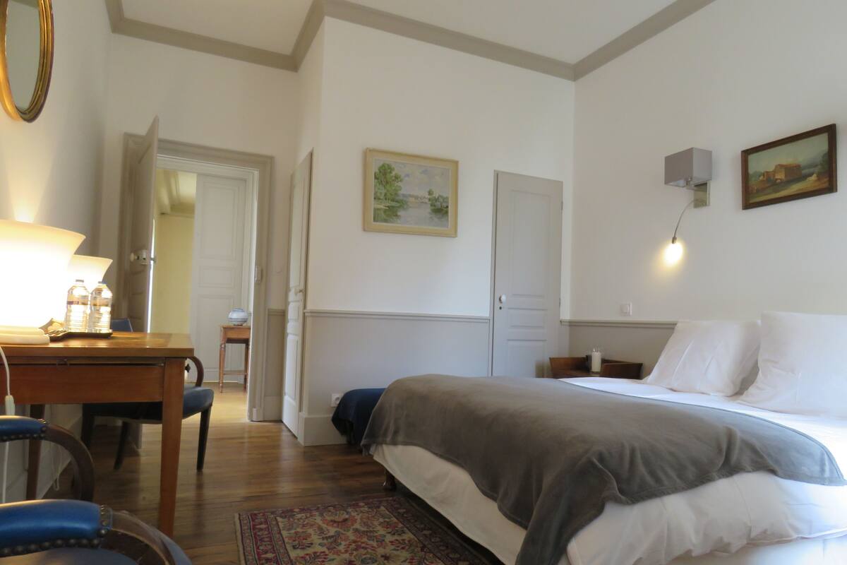Una habitación de hotel con una cama, un escritorio con una lámpara, una silla, una alfombra y un cuadro en la pared.