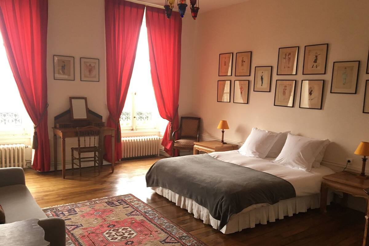 Un dormitorio con cama, escritorio, silla, alfombra y cuadros en la pared.