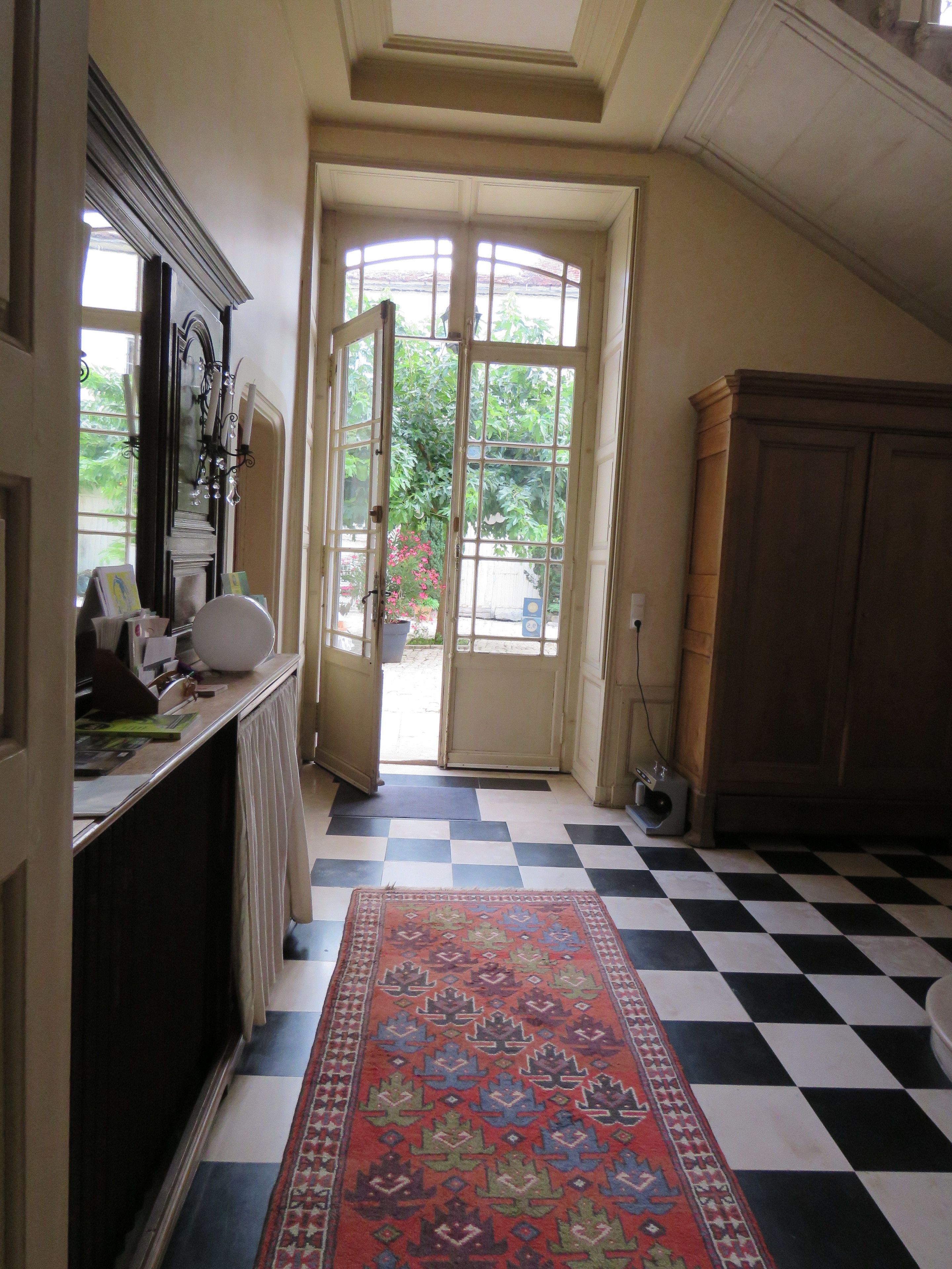 A hallway with a checkered floor, a large rug, and a door leading outside.