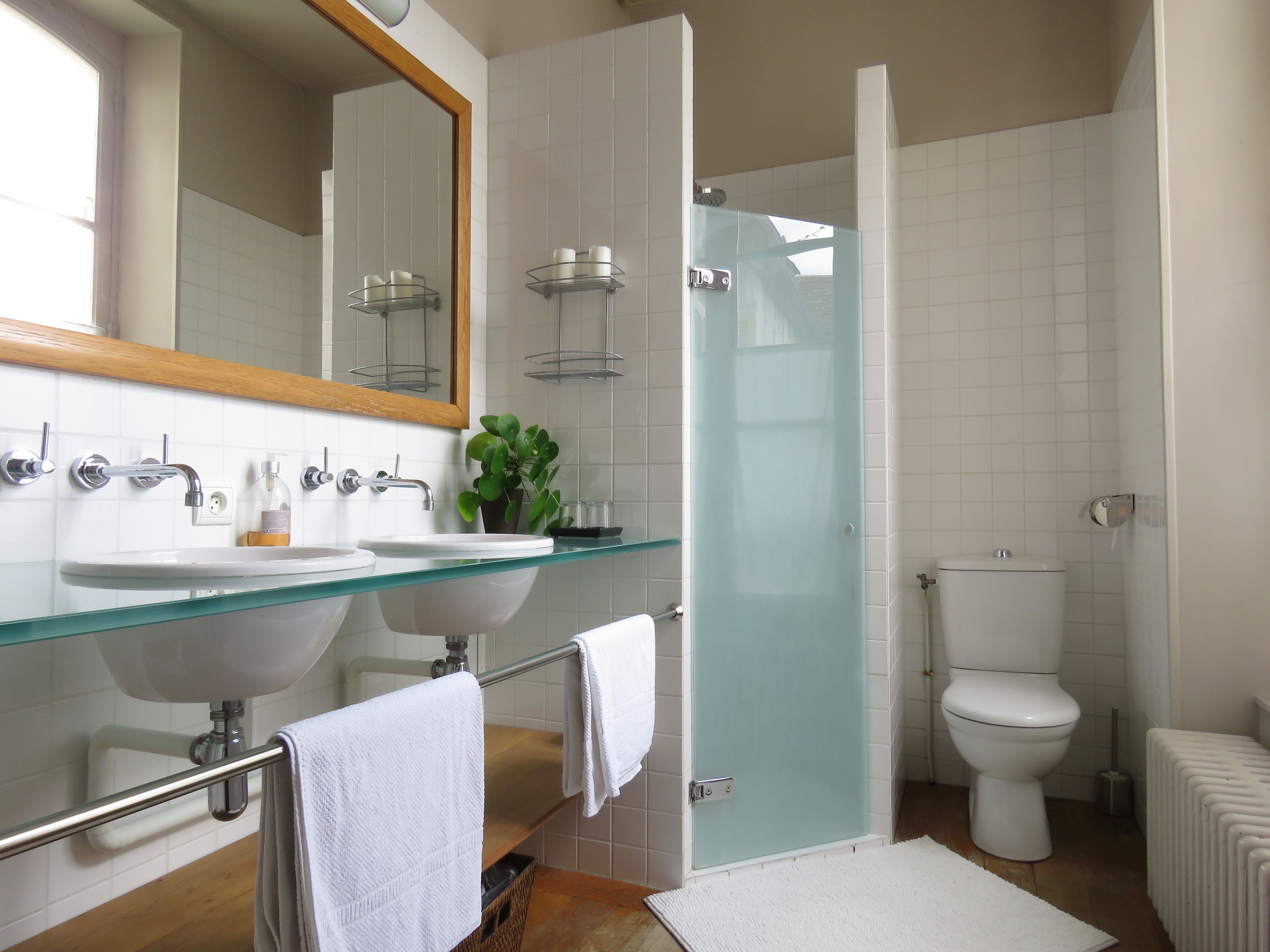 Een moderne badkamer met twee wastafels, een douchecabine van glas, een toilet en een radiator.