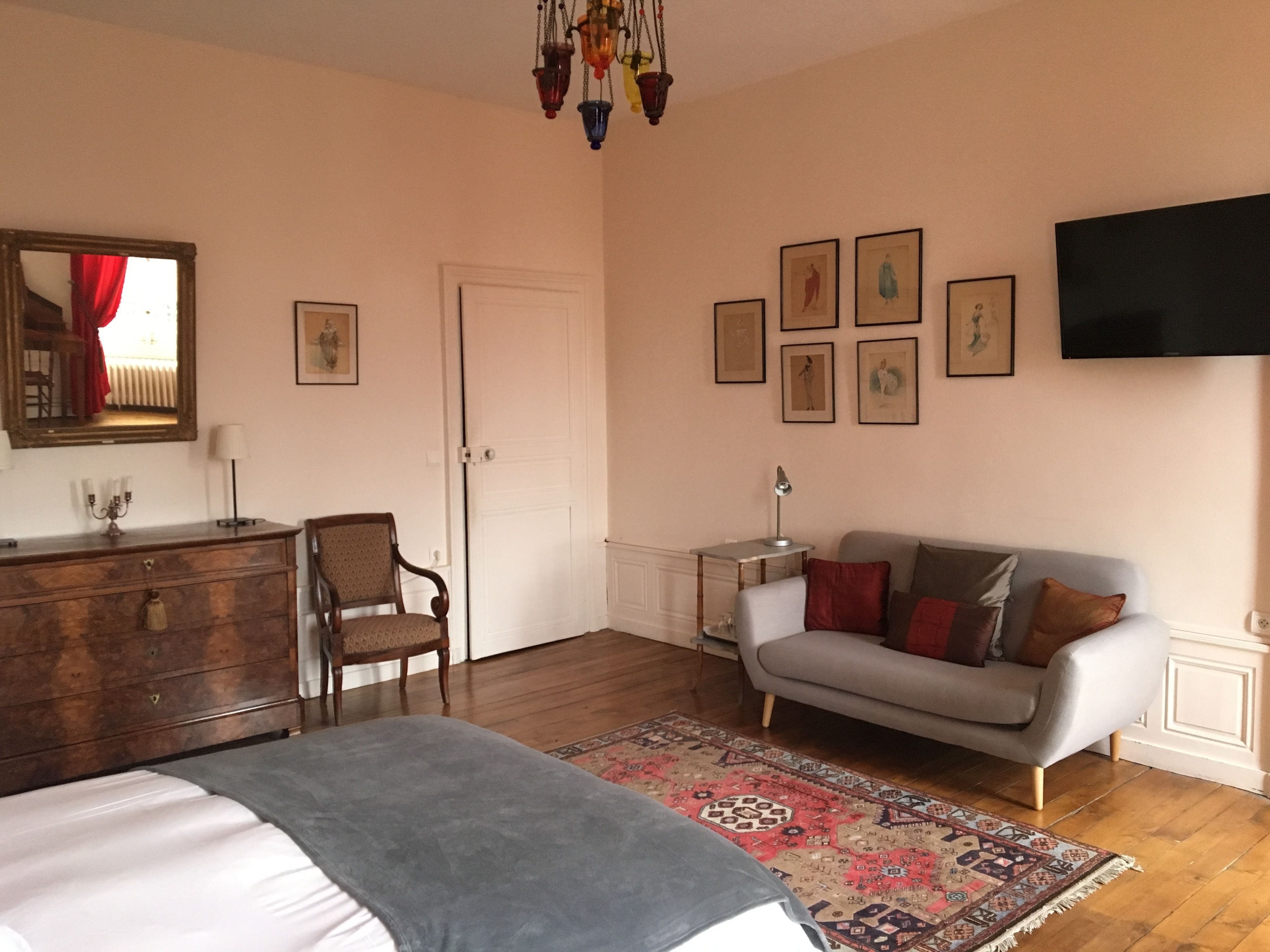 Ein Schlafzimmer mit einem Bett, einem Schminktisch, einem Sessel, einer Couch, einem Fernseher und gerahmten Bildern an der Wand.