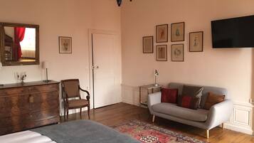 Ein Schlafzimmer mit einem Bett, einem Schminktisch, einem Sessel, einer Couch, einem Fernseher und gerahmten Bildern an der Wand.