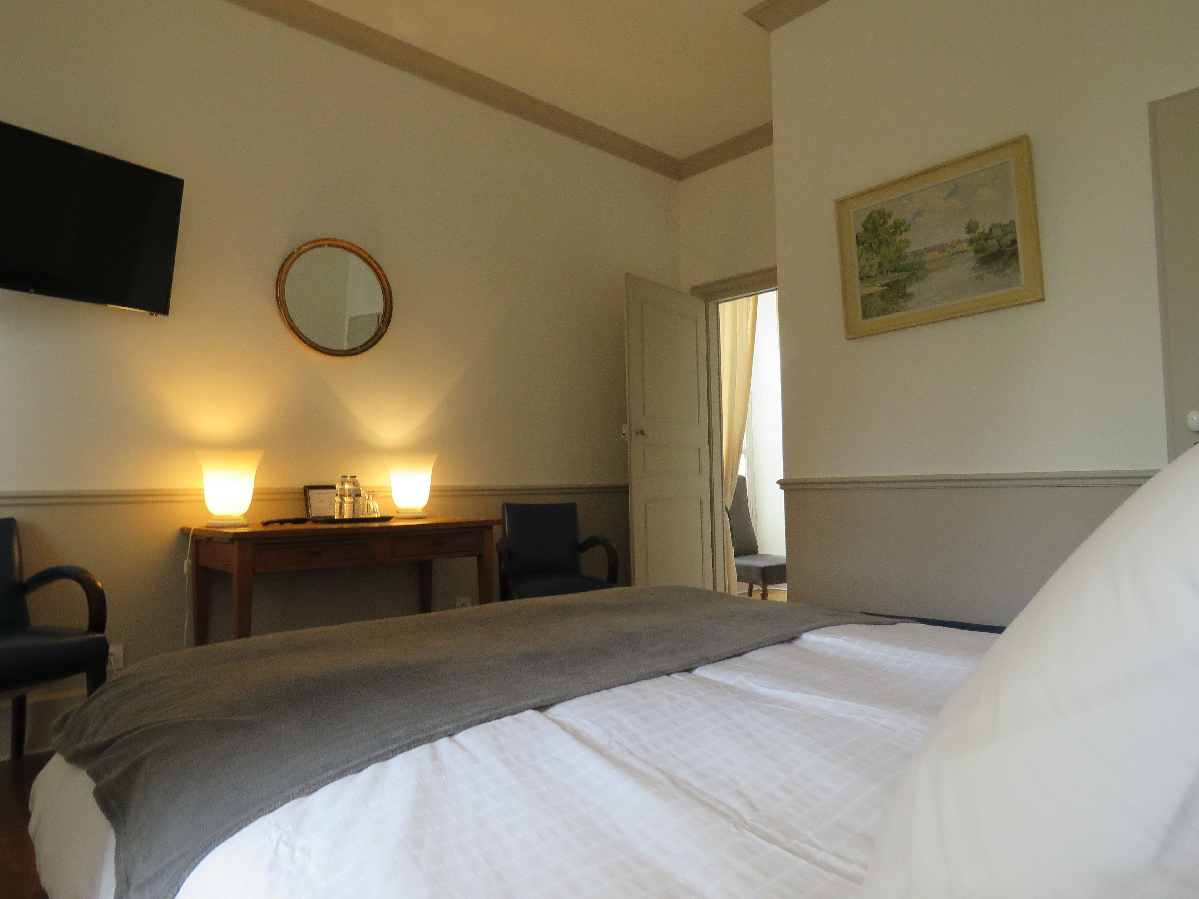 Une chambre d’hôtel avec un lit, un bureau doté de deux lampes, une chaise, un téléviseur et un tableau accroché au mur.