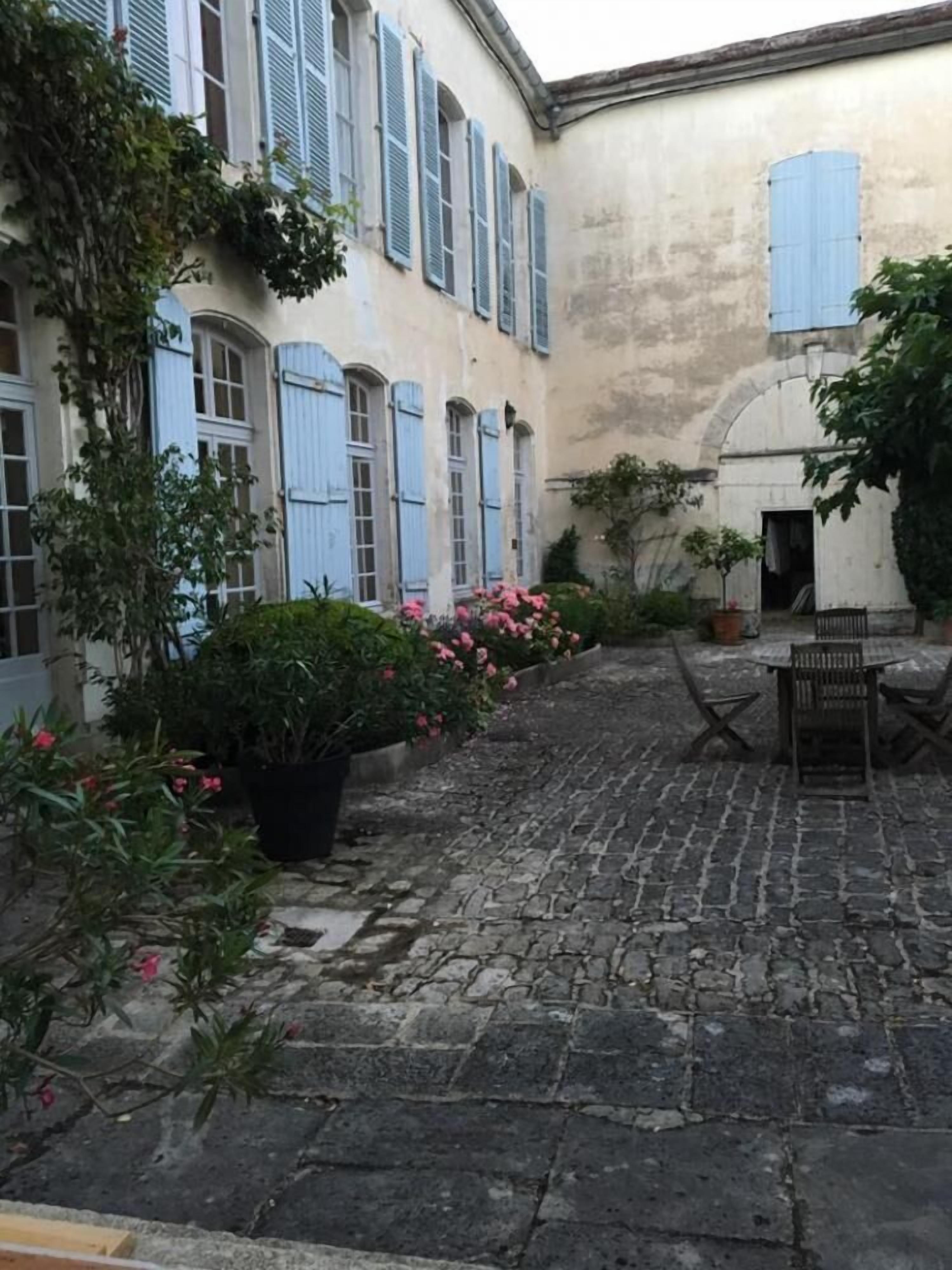A courtyard with a cobblestone path, a wooden bench, and potted plants.