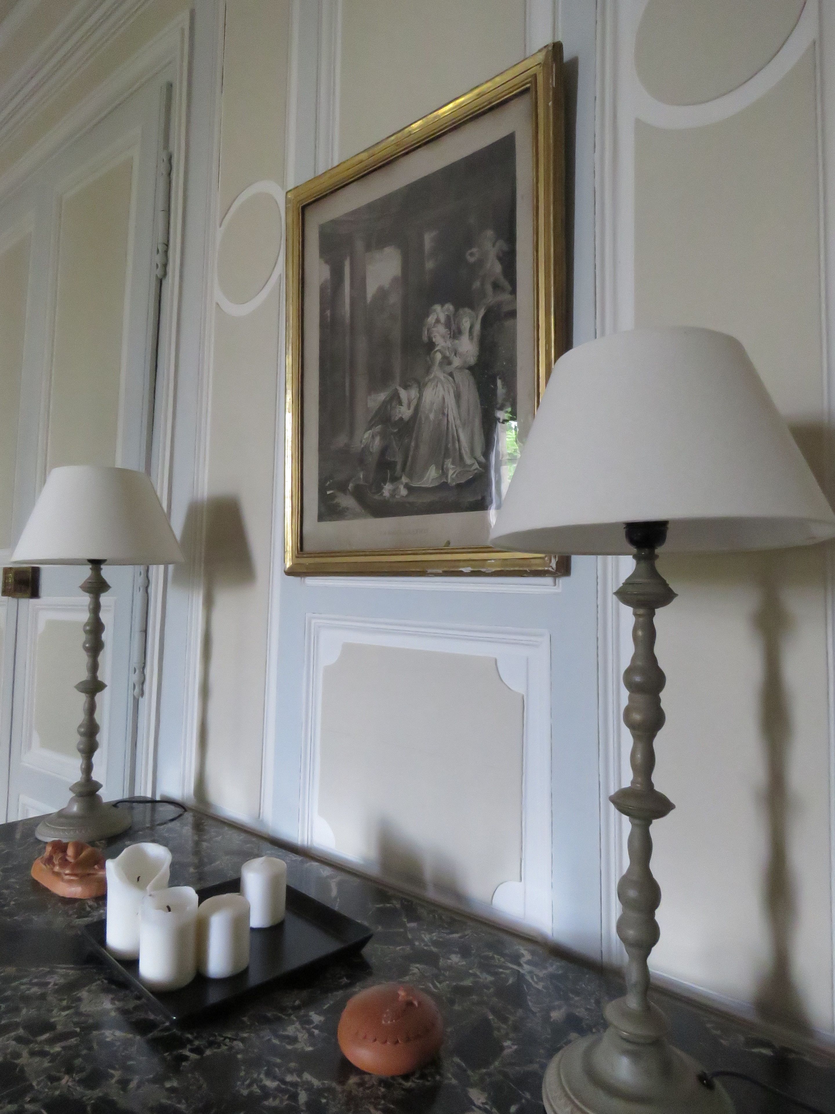 A room with a marble countertop, two table lamps, a framed black and white painting, and a small tray with candles.