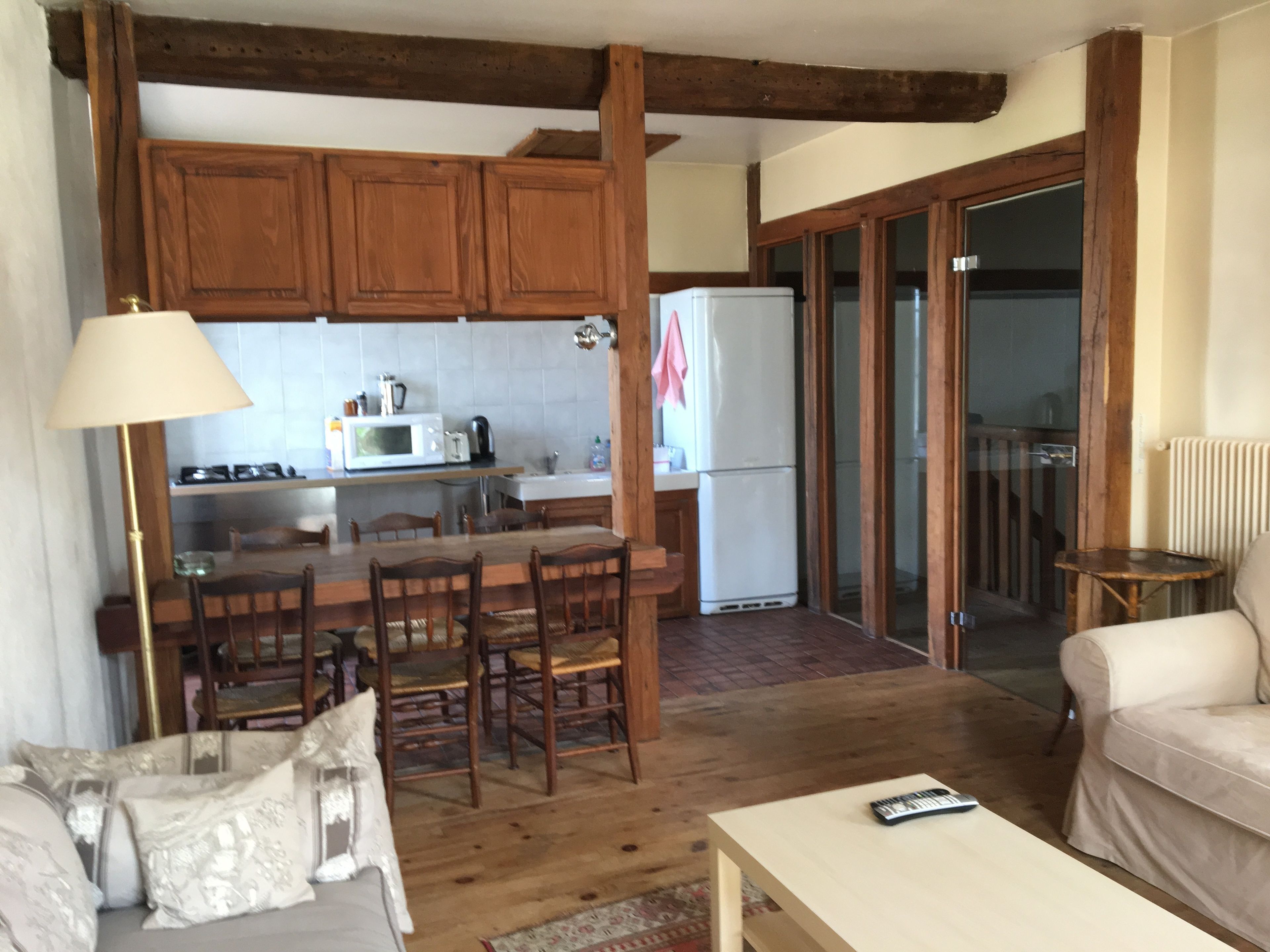 Un salon chaleureux avec un canapé, une table basse et un coin repas comprenant des chaises et une table en bois. La cuisine est équipée de meubles en bois, d’un four à micro-ondes et d’un réfrigérateur.
