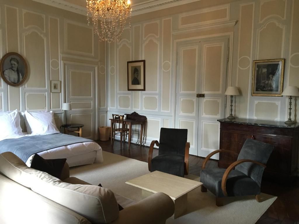 A hotel room with a bed, a sofa, a coffee table, two armchairs, a desk, and a chandelier.