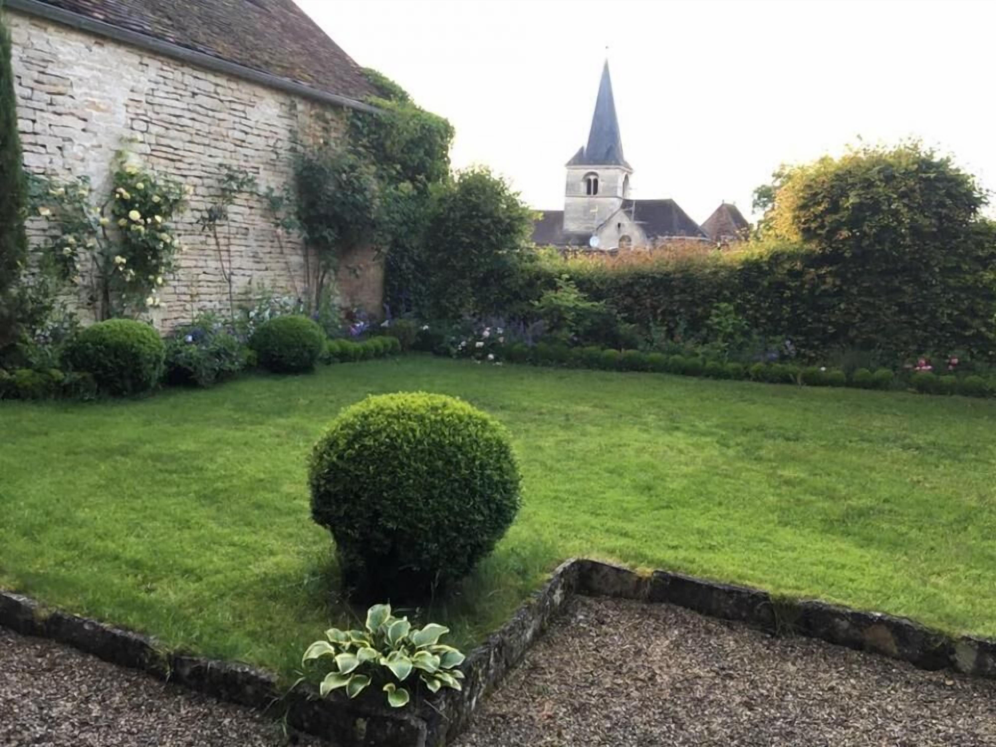A well-maintained garden with a stone building and a church steeple in the background.