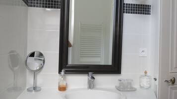 A bathroom with a white sink, a large mirror, two wall-mounted lights, a small glass container, and a towel rack.
