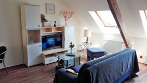 A modern living room with a flat-screen TV, a glass coffee table, a blue sofa, and a skylight. - Gelder Dyck (Kevelaer)