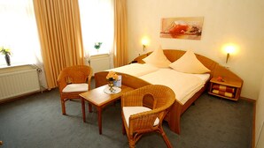 A hotel room with a bed, two chairs, a small table with a vase of flowers, and a painting on the wall. - Gelder Dyck (Kevelaer)