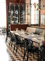 A restaurant with checkered flooring, black chairs, and tables set with wine glasses and plates.