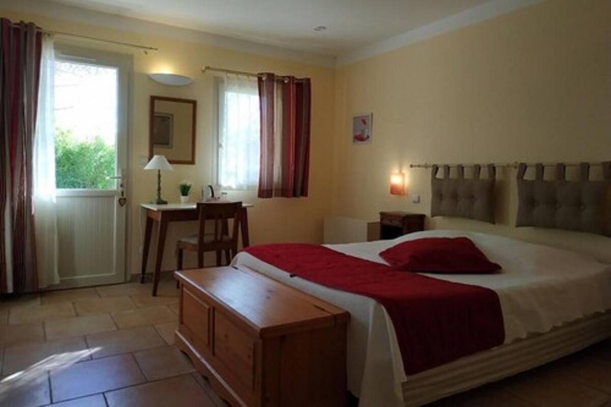 Une chambre à coucher avec un lit, un bureau, une chaise et une fenêtre avec des rideaux.