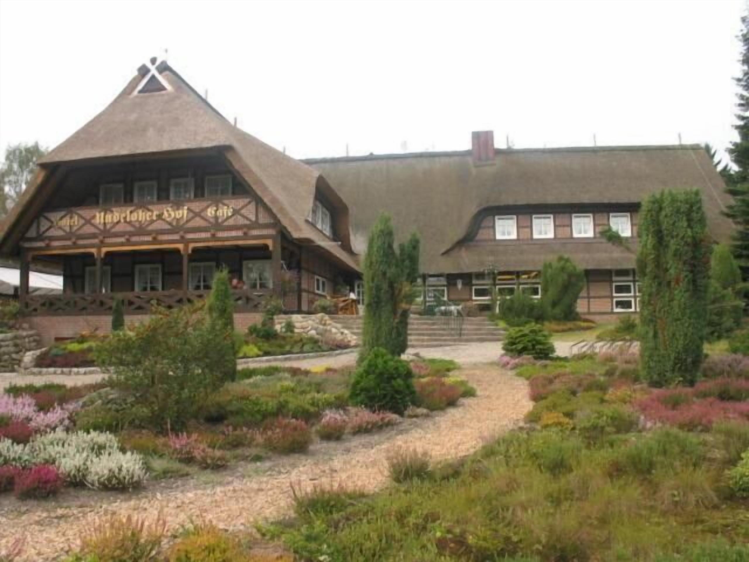 A traditional building with a steeply pitched roof and a thatched roof section, surrounded by a landscaped garden with various shrubs and a gravel path.