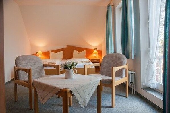 A cozy room with a bed, two bedside tables with lamps, a small table with a chair, and a window with curtains. - Undeloher Hof (Undeloh)