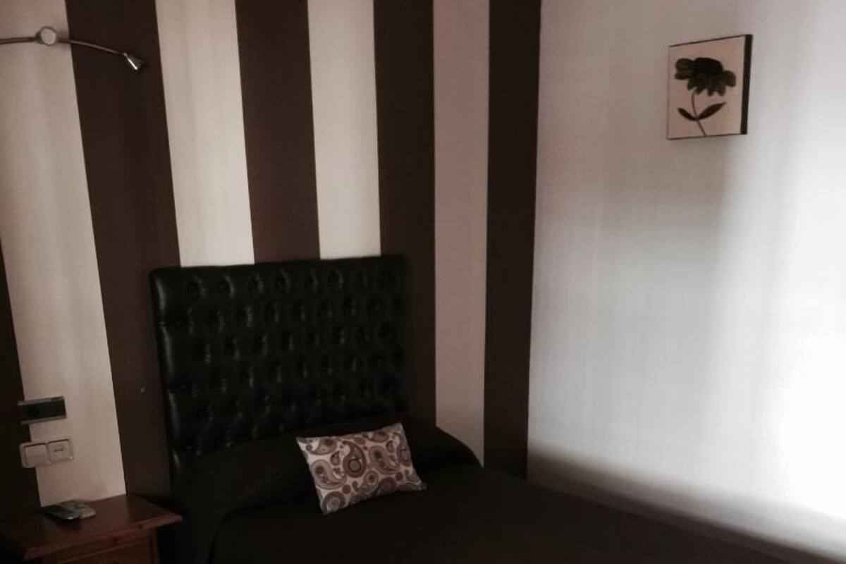 A bedroom with a bed, a nightstand, a lamp, and a wall-mounted picture.