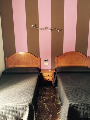 Una habitación con dos camas individuales, una mesita de noche y una lámpara fijada a la pared.