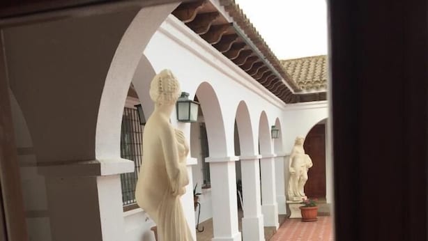 Ein überdachter Innenhof mit weißen Bögen, Statuen, Fliesenboden und Topfpflanzen.