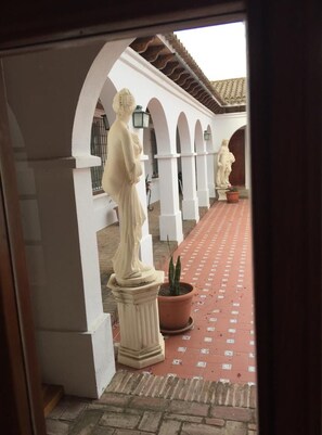Ein überdachter Innenhof mit weißen Bögen, Statuen, Fliesenboden und Topfpflanzen.