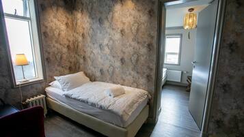 A bedroom with a bed, a chair, a radiator, and a view of another room through an open door.