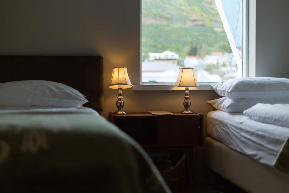 A bedroom with two beds, each with white linens, and two bedside lamps.