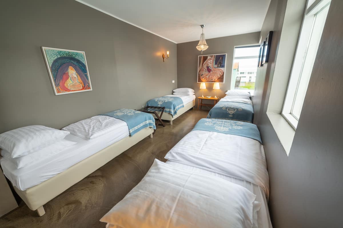 A hotel room with two single beds, a small table with two lamps, and artwork on the walls.