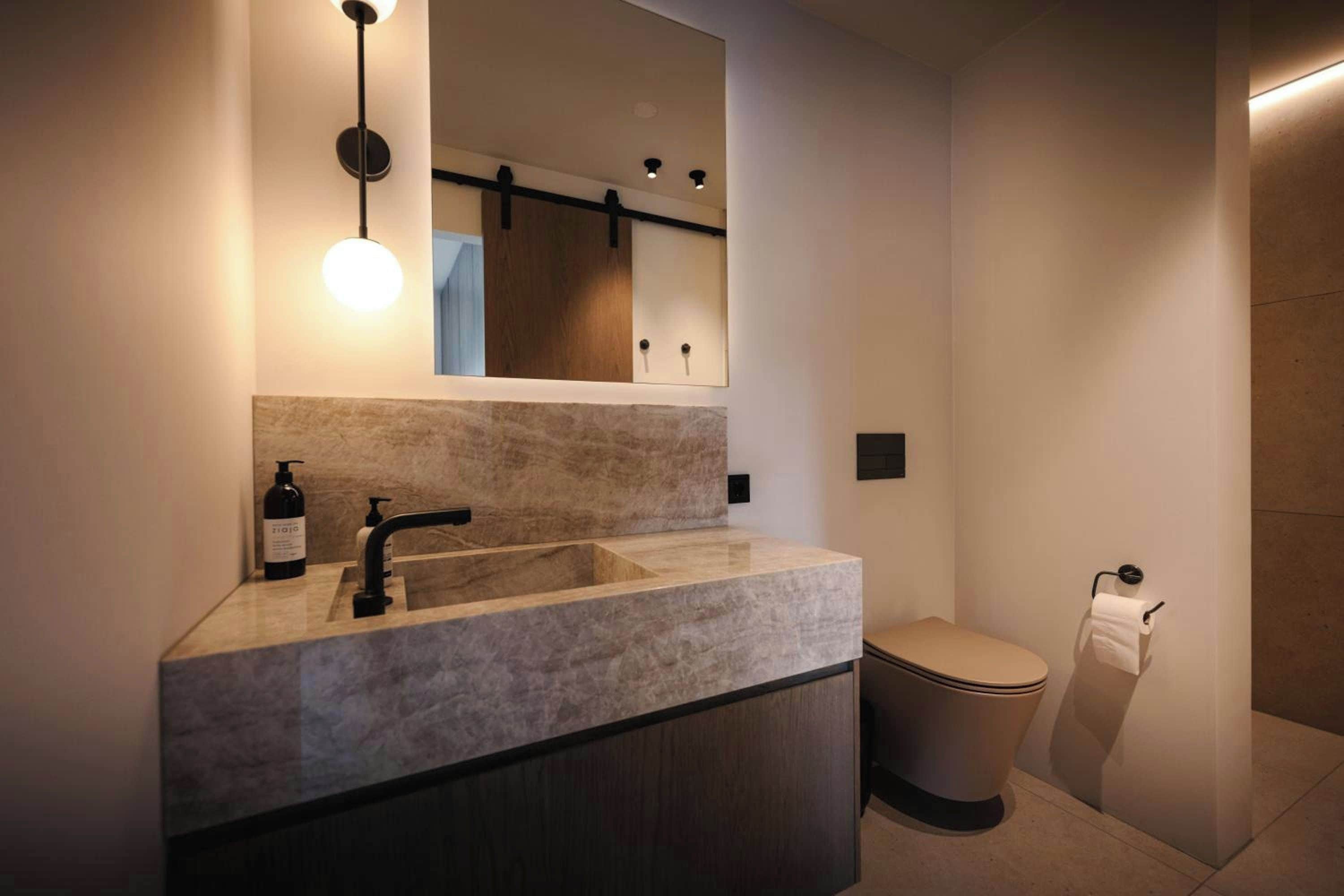 Ein modernes Badezimmer mit einem мраморный Waschbecken, einem Spiegel und einer Toilette.
