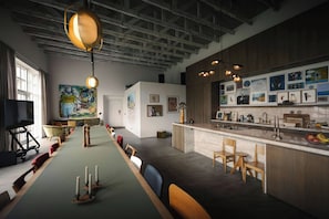 A modern kitchen with a long dining table, wooden chairs, and a variety of artwork on the walls.