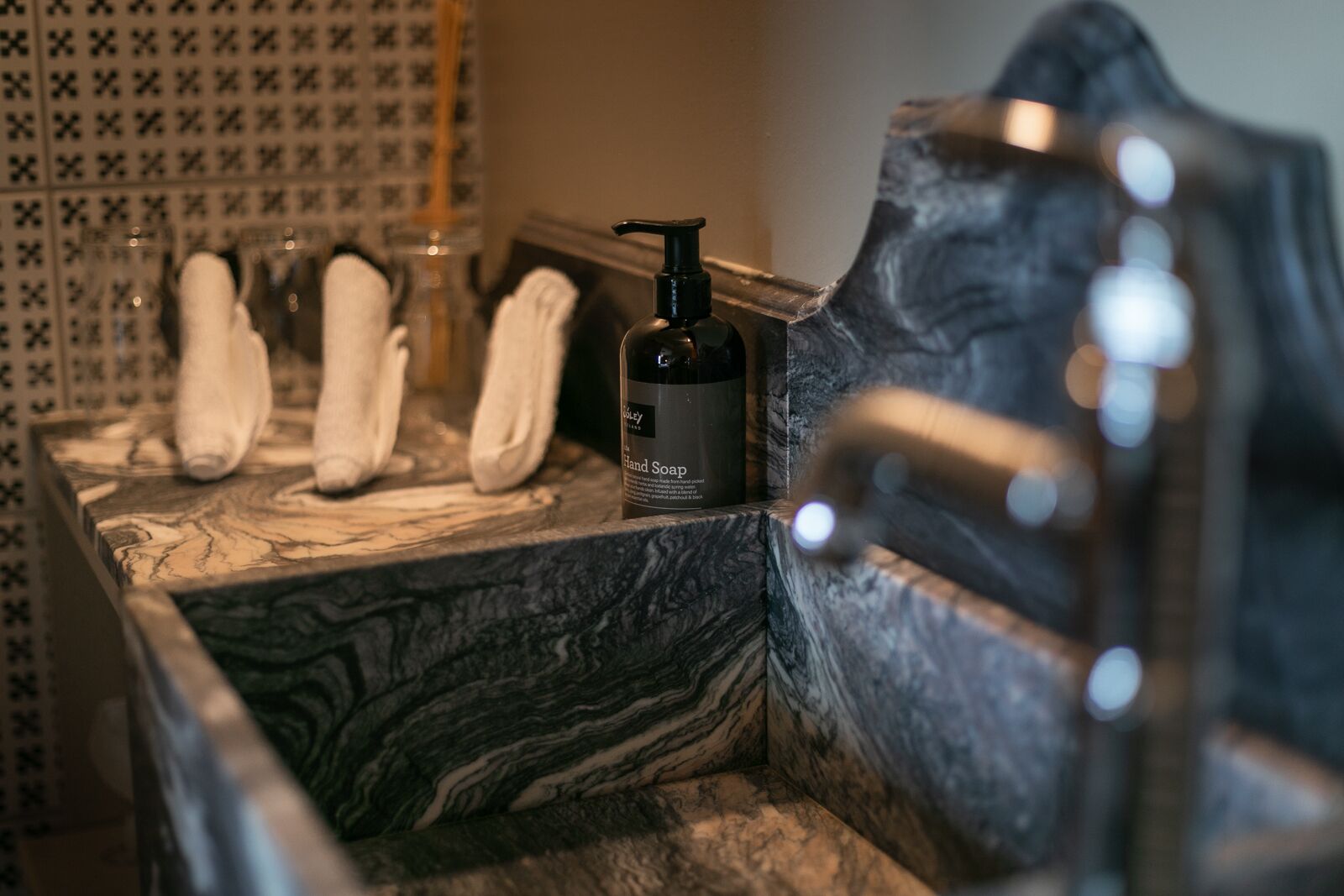 Un baño con lavamanos de mármol, dispensador de jabón para manos y un perchero con toallas.