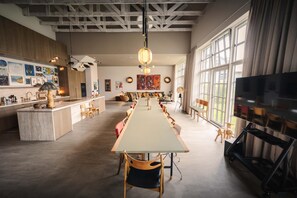 A spacious living area with a long dining table, multiple seating arrangements, and a large window providing natural light.