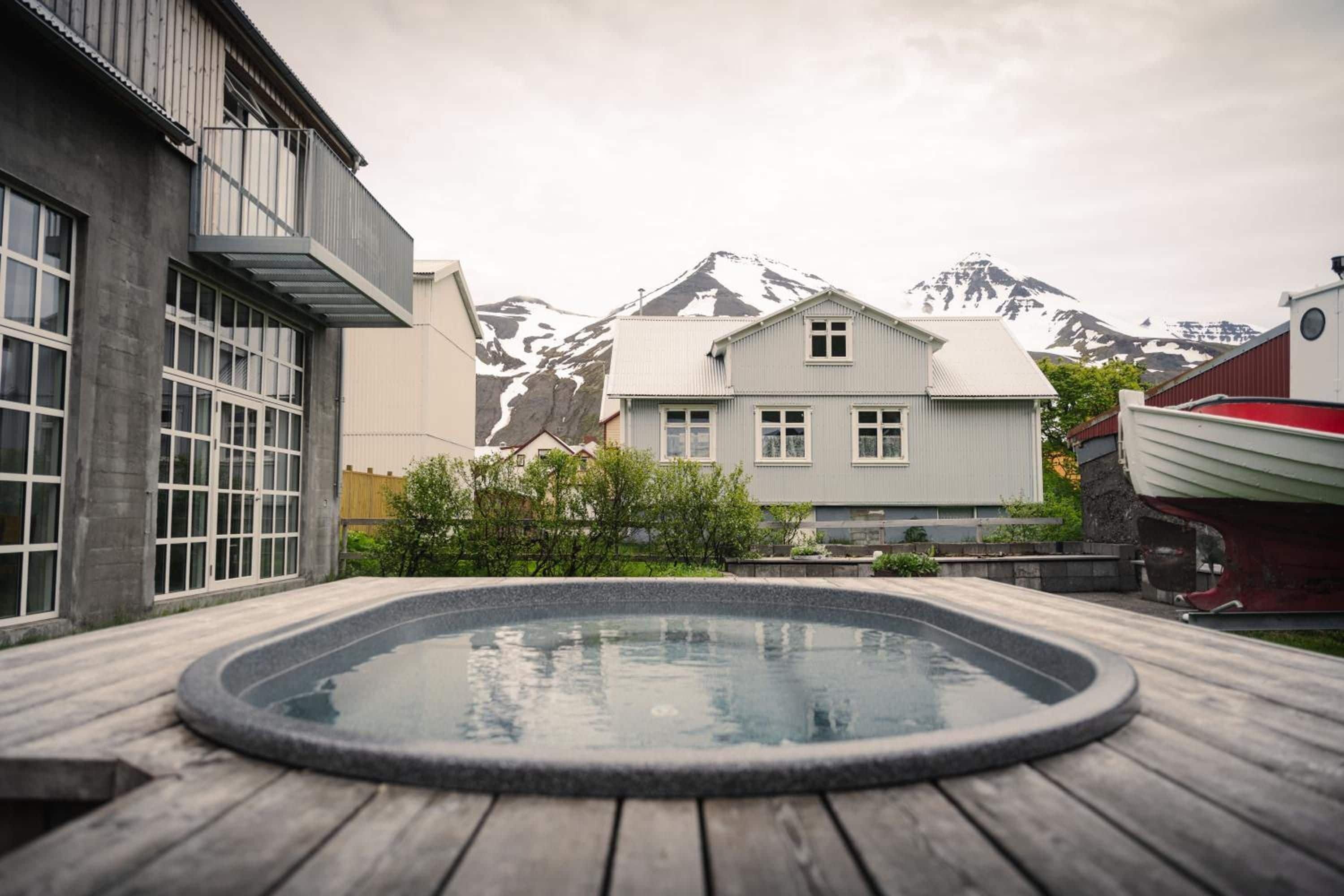 A wooden deck with a hot tub, a building with large windows, and a mountain in the background.