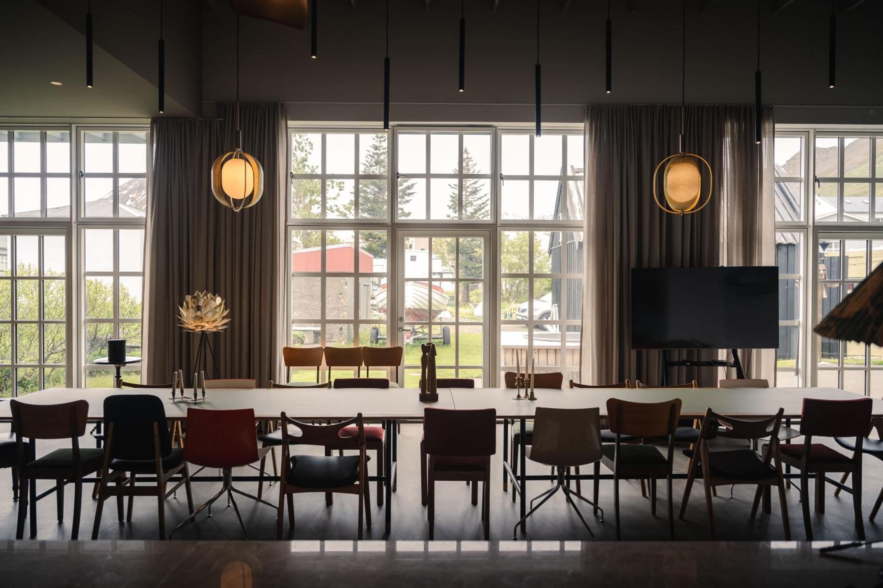 A conference room with a long table, chairs, a large window with curtains, and a flat-screen TV.