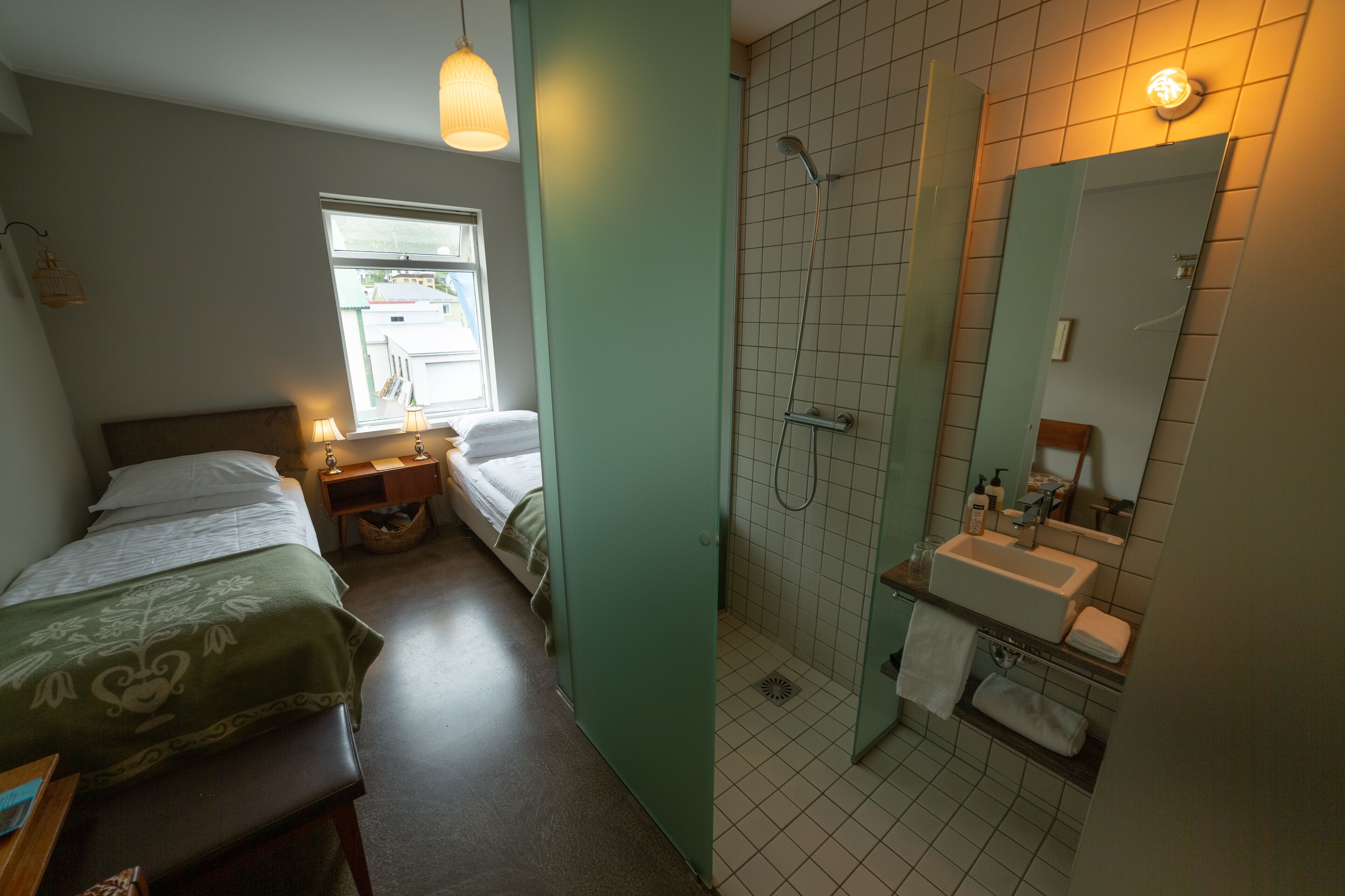 Un dormitorio con cama, mesita de noche y ventana. La habitación tiene una puerta verde y una ventana pequeña.