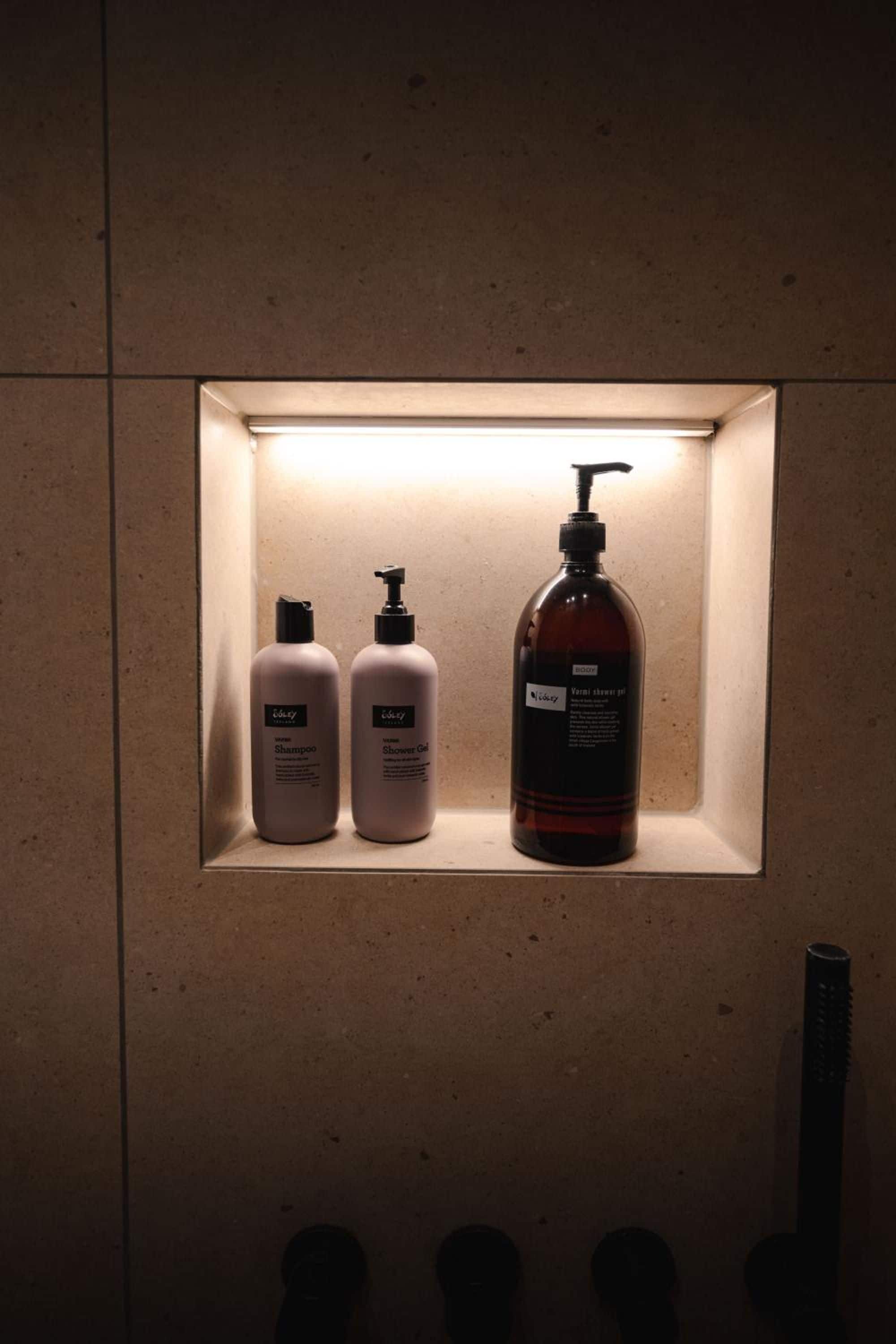 Un estante de baño con tres botellas de productos de aseo: dos para champú y gel de ducha, y una para jabón corporal.