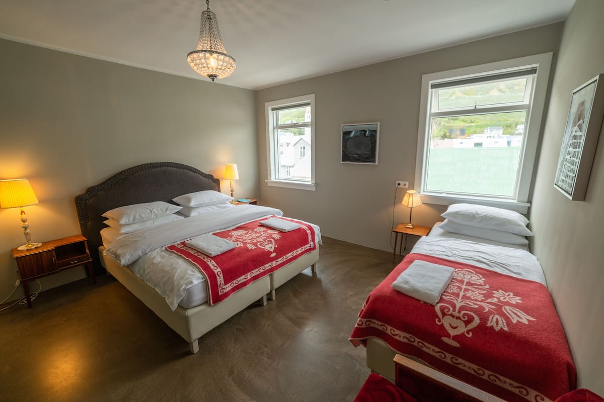 A bedroom with two beds, a chandelier, and two bedside tables with lamps.