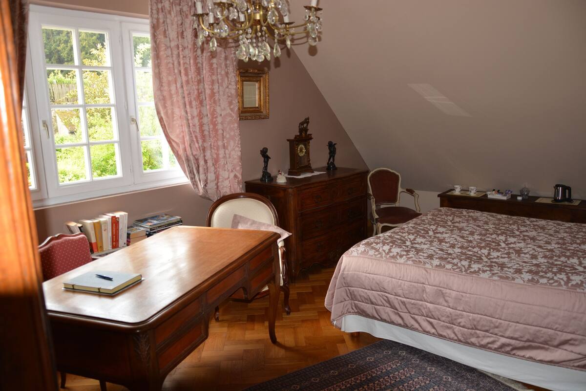 Een slaapkamer met een houten bureau, een bed met een bloemenprint, een dressoir en een stoel.