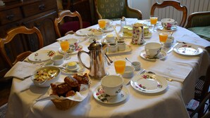 Una mesa de desayuno preparada con platos, tazas, una jarras y una cesta de pasteles.