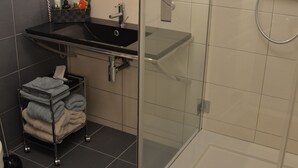 Un baño moderno con ducha de vidrio, lavamanos negro y un perchero para toallas.