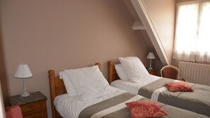 Un dormitorio con dos camas, una mesita de noche con lámpara, una silla y un ventanal con cortinas.