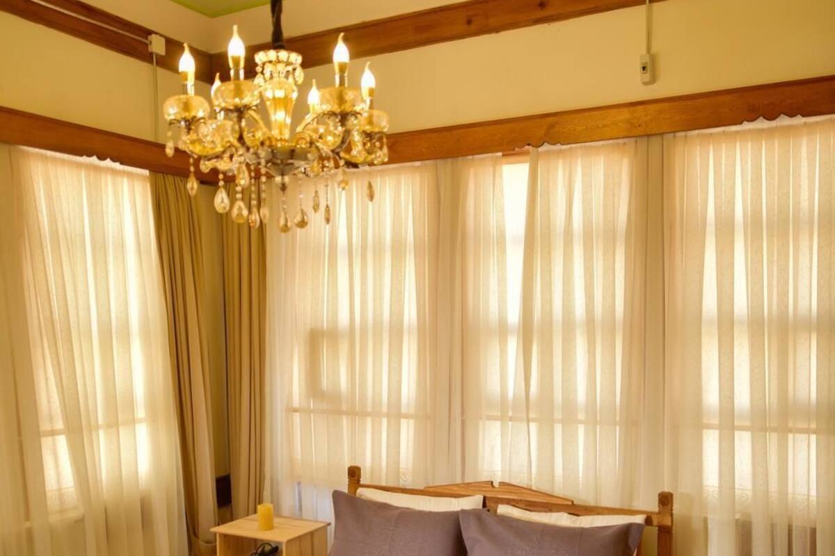 A bedroom with a large bed, wooden headboard, a chandelier, and curtains.