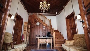 A wooden staircase leading to a second floor, a wooden desk with a computer, two patterned armchairs, and a chandelier. - Cifte Konak Butik Otel (Amasya)